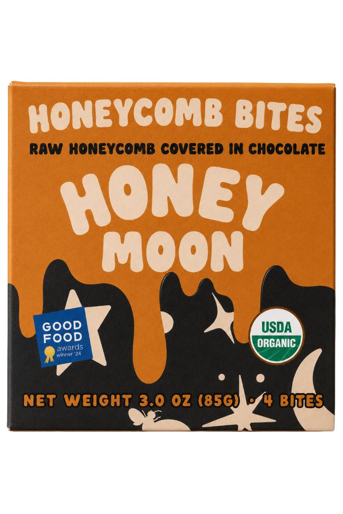 A square box of Honeycomb Bites 'Honey Moon' chocolate-covered honeycomb bites. The packaging features a warm orange background with cream-colored bubbly text, black silhouettes of bees, and a blue Good Food Awards 2024 badge on the bottom left.